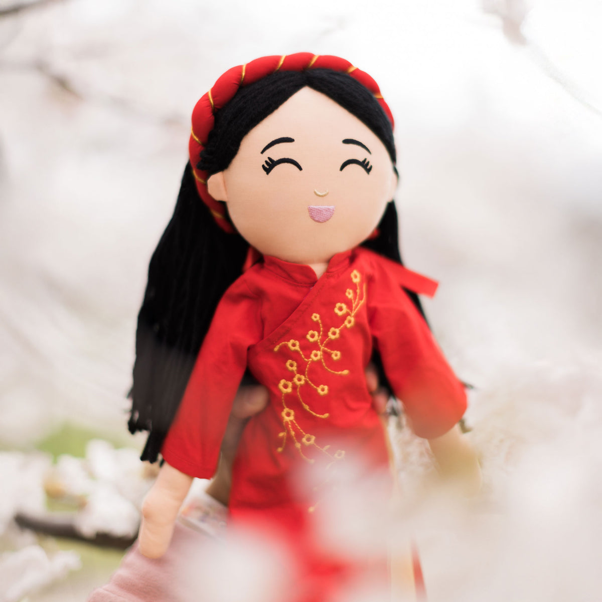 Joeydolls Hoa Vietnamese doll in a red áo dài outdoors with soft flowers behind her