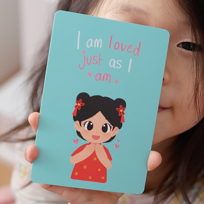 Child holding an affirmation card that reads “I am loved just as I am”