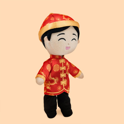 Side profile of the Chinese Boy Cultural Mini Doll showcasing a traditional red tang jacket with gold dragon motifs, black pants, and a coordinating festive hat.
