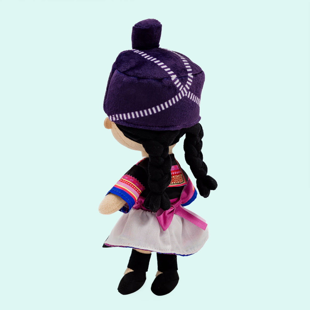 Side view of Maiv, a soft plush Hmong Cultural Mini Doll wearing a traditional Hmong-inspired outfit with colorful patterns, braided hair, a Hmong head wrap, and a pink waist sash.
