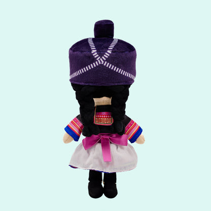 Back view of Maiv, a soft plush Hmong Cultural Mini Doll showing her braided hair, traditional Hmong head wrap, pink ribbon sash, and colorful patterned skirt inspired by traditional Hmong clothing.