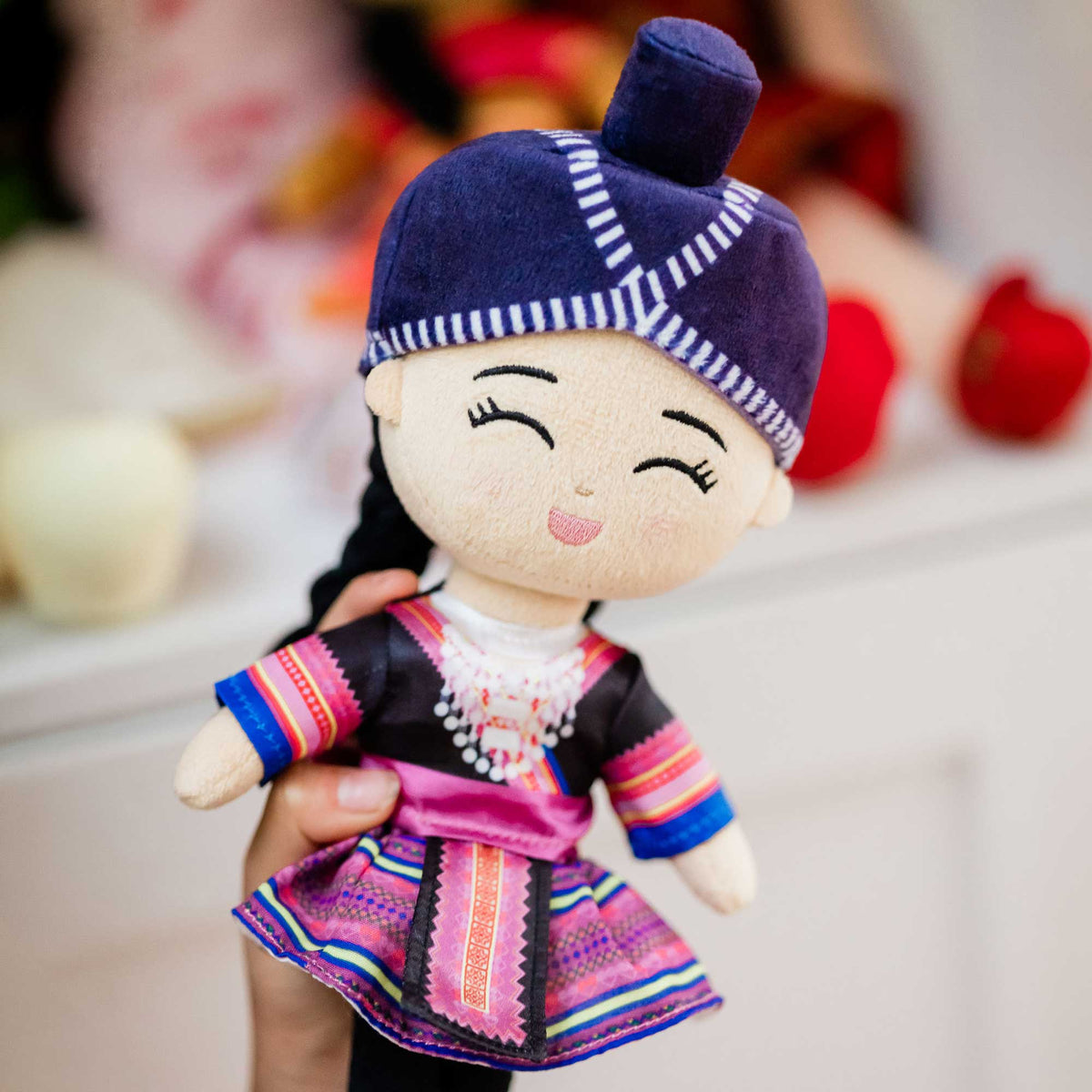 Hand holding Joeydolls Maiv Hmong doll showing the colourful side of her reversible skirt