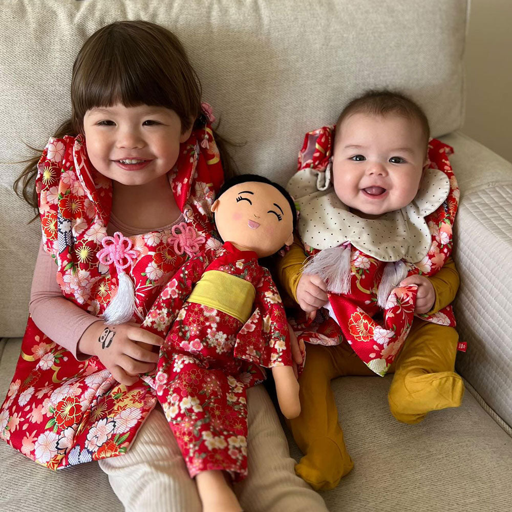 Two smiling children in red kimonos with Aiko, the Joeydolls 18-inch Japanese doll