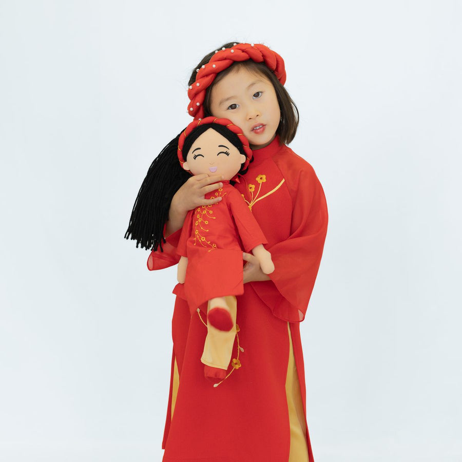 Child in a red áo dài by Ao Dai by Cute Sass hugging Joeydolls Hoa in her matching red áo dài