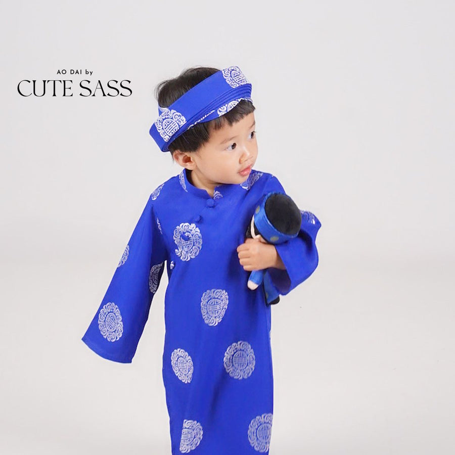 Boy in a royal blue áo dài and khăn đóng by Ao Dai by Cute Sass, holding his matching Minh doll
