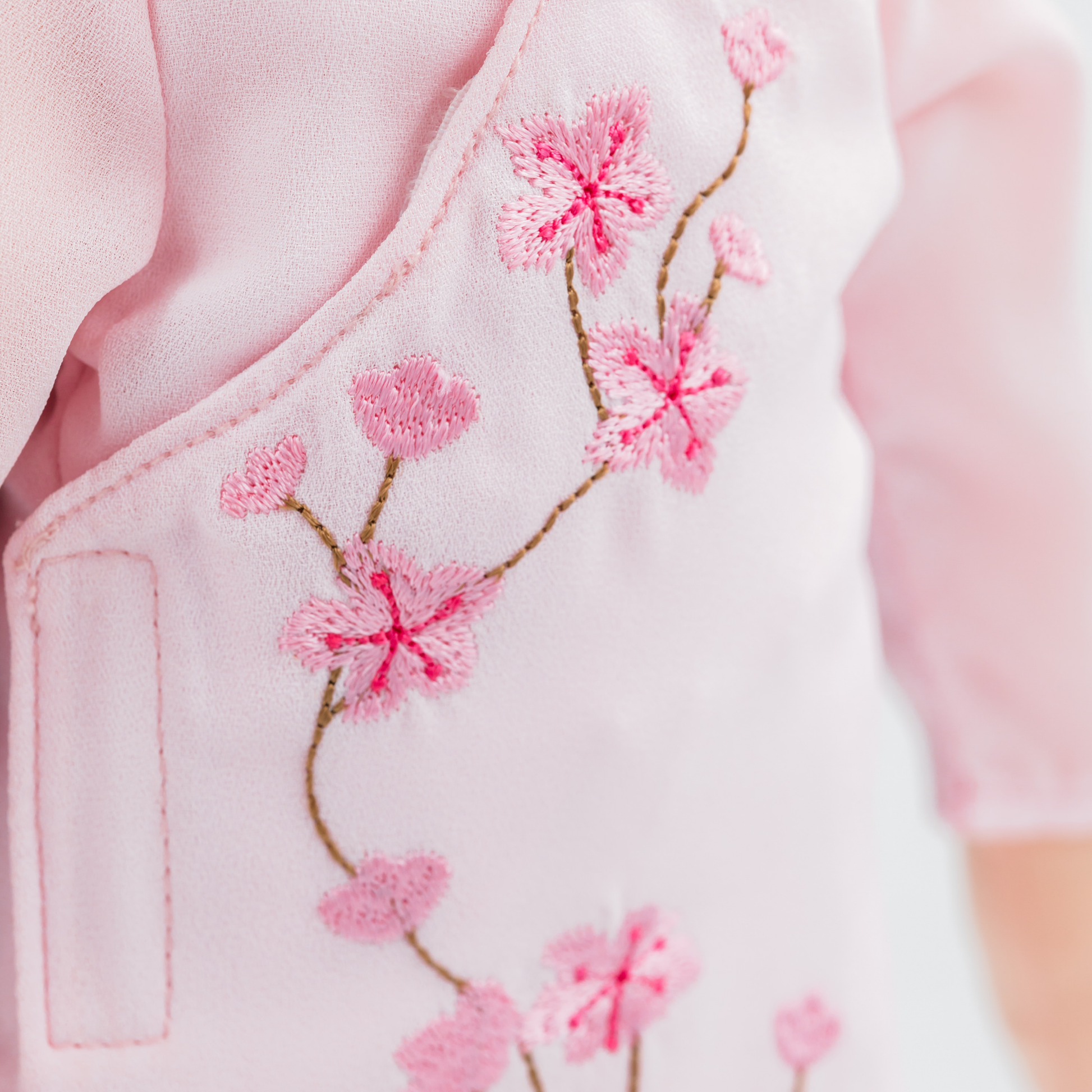 Close-up of cherry blossom embroidery on a pink áo dài worn by Thuong Vietnamese cultural doll