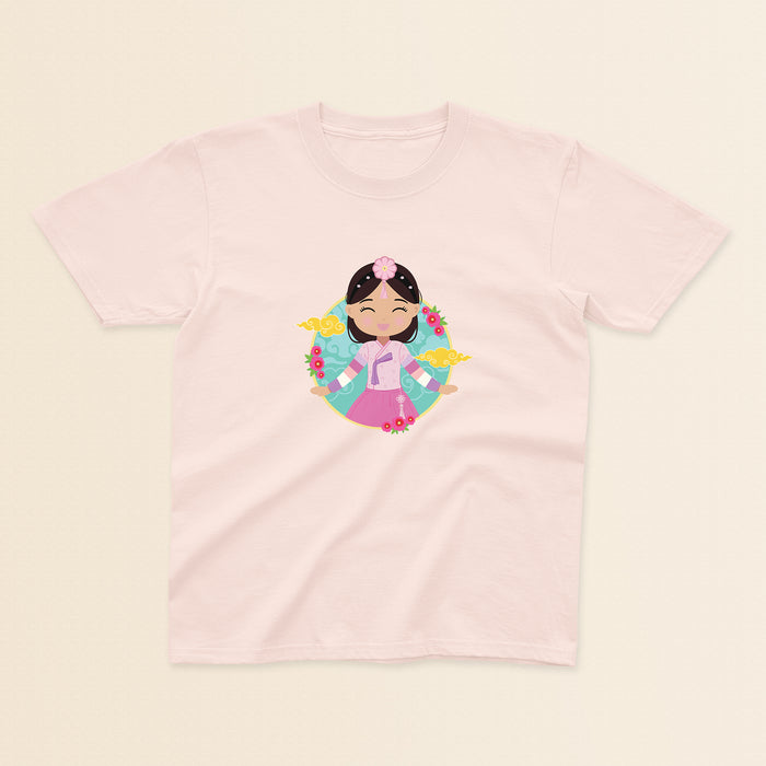 Korean Cultural Celebration baby and kids t-shirt in light pink with a graphic of a smiling girl with long hair adorned with a daenggi ribbon and a jokduri headpiece, wearing a pink hanbok with a norigae ornament, set against a circular background with floral elements and traditional patterns.