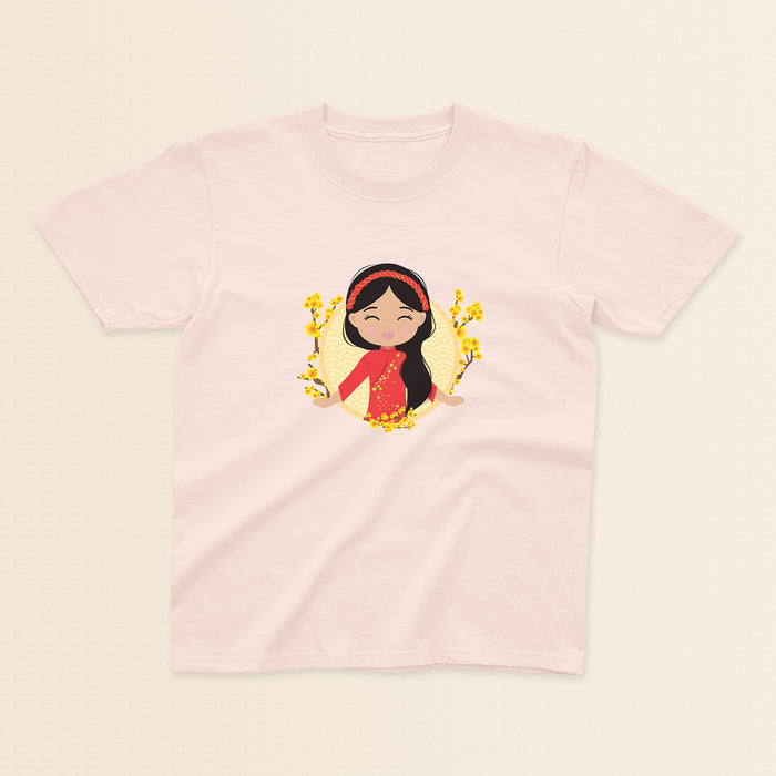 Vietnamese Cultural Celebration baby and kids tee in light pink featuring a printed illustration of a smiling girl with long black hair, wearing a red áo dài featuring delicate mai flower details and a traditional khăn đóng headpiece, set against a circular yellow background with floral elements.