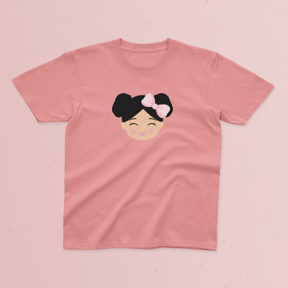 A pink short-sleeve t-shirt with a Joeydolls Icon with black hair in a double bun and a pink bow, displayed flat on a textured pink background.