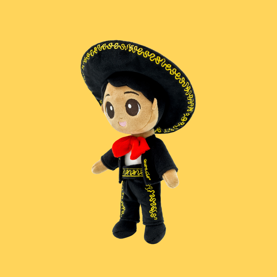 Meet Mateo 🎸 — a name loved across Mexico and beyond. Wearing his traditional Mariachi suit and hat, he celebrates family, music, and the warmth of shared culture and connection. Side angle of a plush Mexican boy doll with gold embroidered details, red bow tie, and large sombrero on a yellow background.