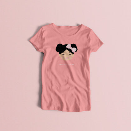 Proudly Asian women’s t-shirt in pink featuring a printed illustration of a smiling girl’s face with black hair in two buns and a bow, with the text “PROUDLY ASIAN” below.