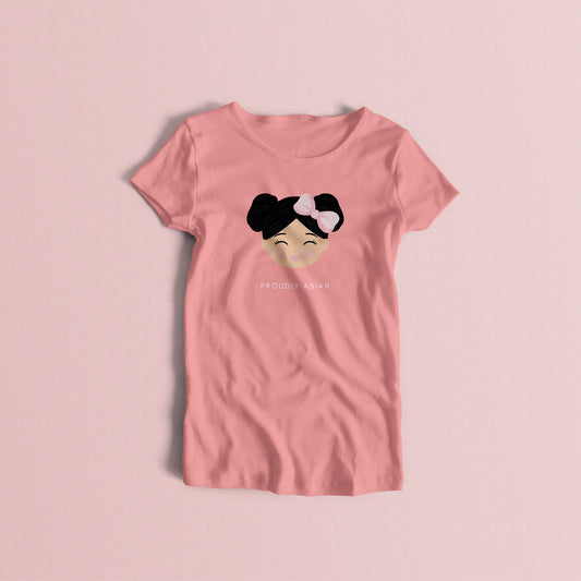Proudly Asian women’s t-shirt in pink featuring a printed illustration of a smiling girl’s face with black hair in two buns and a bow, with the text “PROUDLY ASIAN” below.