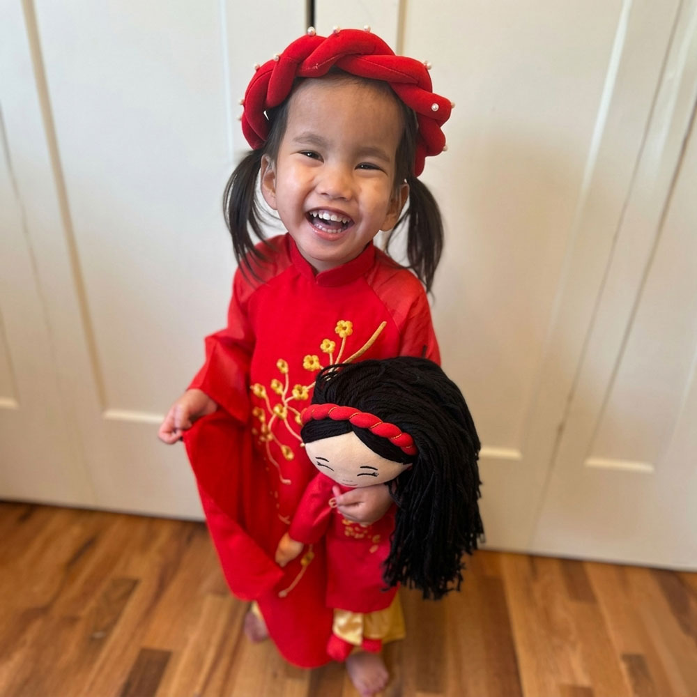 Smiling child holding a Hoa Vietnamese cultural doll, both wearing red áo dài