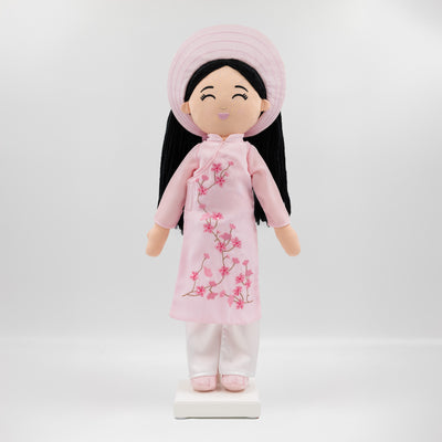 Thuong Vietnamese cultural doll wearing a pink áo dài with cherry blossom embroidery, white satin pants, and a pink khăn đóng headdress