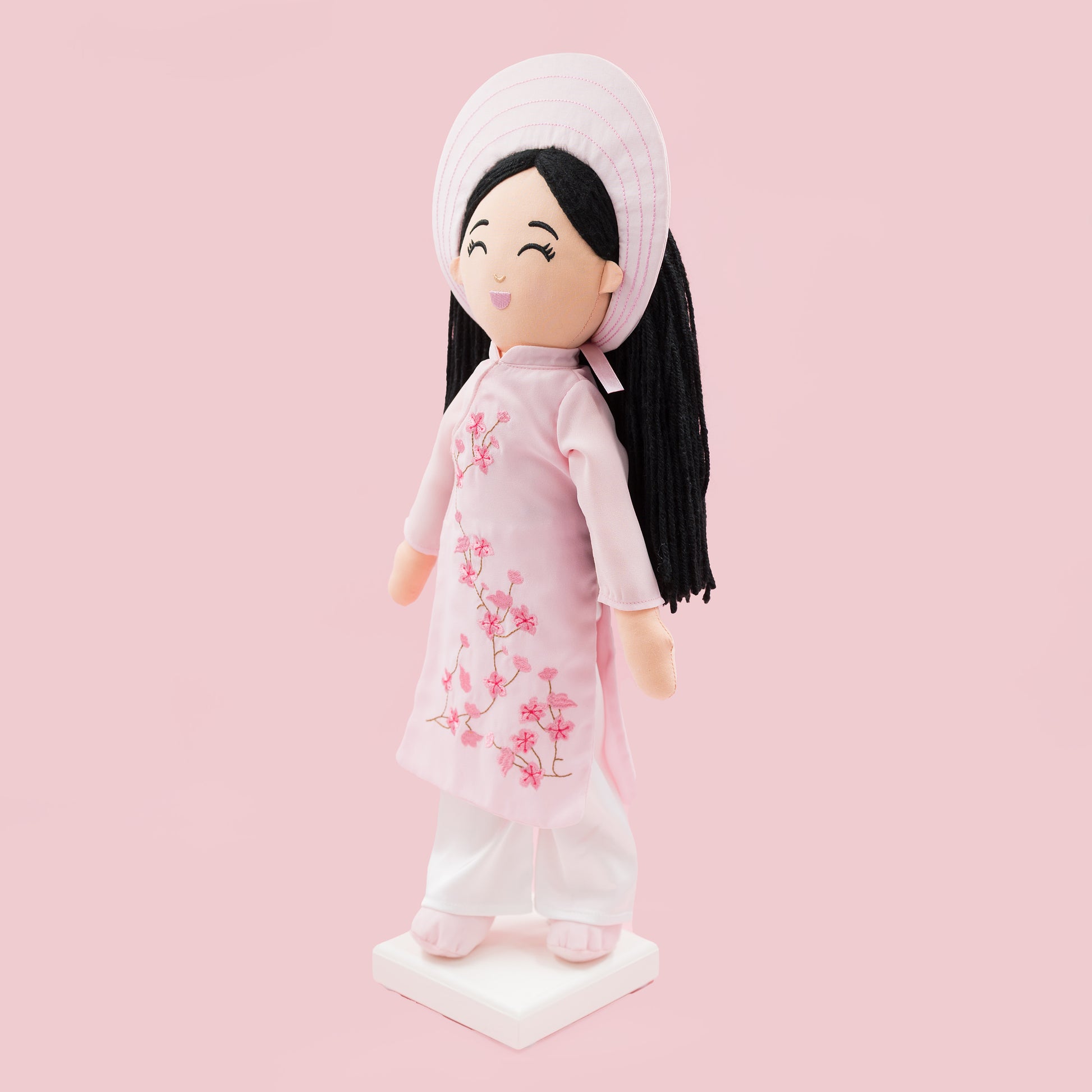 Angled view of Thuong Vietnamese cultural doll in a pink áo dài with cherry blossom embroidery and white pants