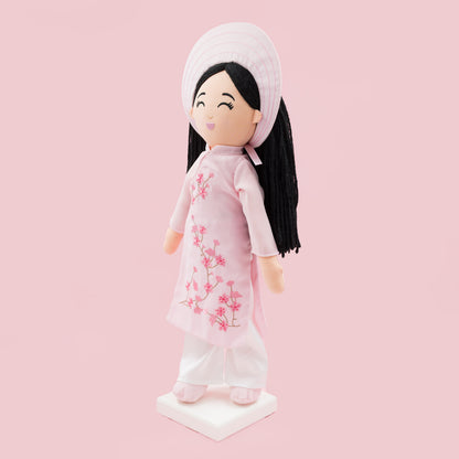 Angled view of Thuong Vietnamese cultural doll in a pink áo dài with cherry blossom embroidery and white pants