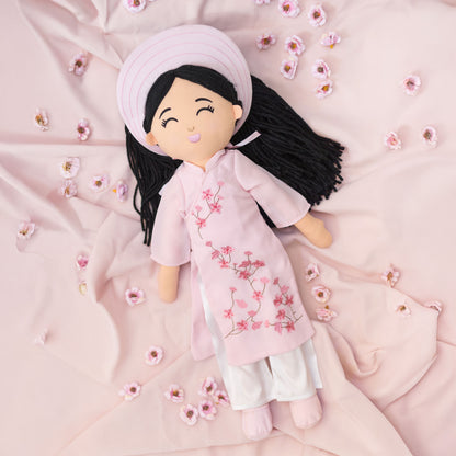 Thuong Vietnamese cultural doll in a pink áo dài surrounded by soft fabric and floral accents