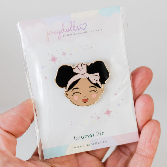 Joeydolls Cheerful Jasmine gold enamel pin on a Joeydolls card, held in hand to show the smiling girl character with double buns and a pink headband.
