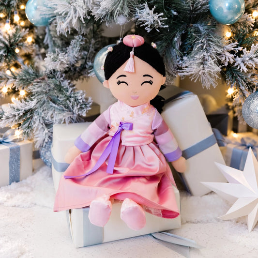 Danbi Korean plush doll in a pink hanbok, seated on a gift beneath a frosted Christmas tree.