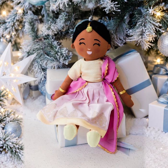 Kamala Indian plush doll in a pink and gold outfit with gold jewellery, seated among Christmas gifts.