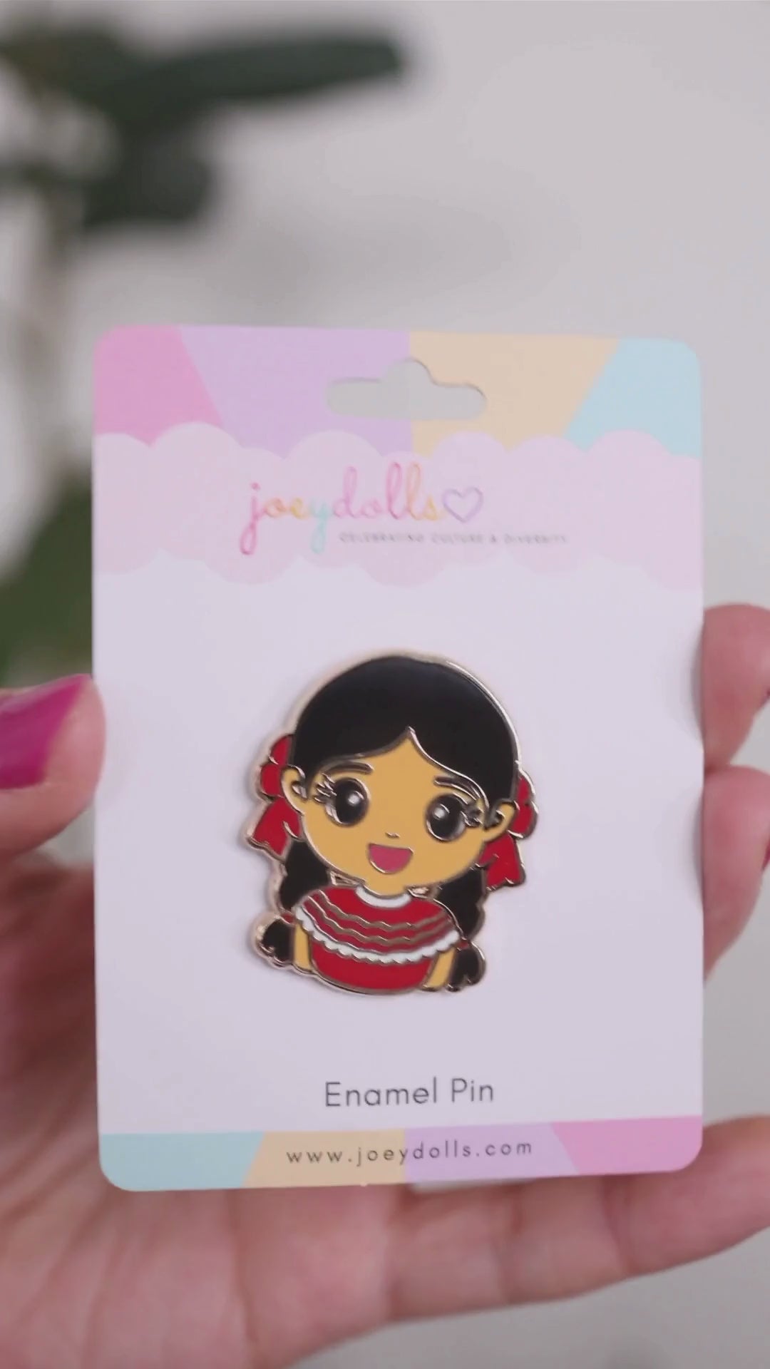 Joeydolls Mexican Xochitl gold enamel pin on branded packaging, featuring a smiling girl in a red folklórico dress with braided pigtails and red ribbon accents.