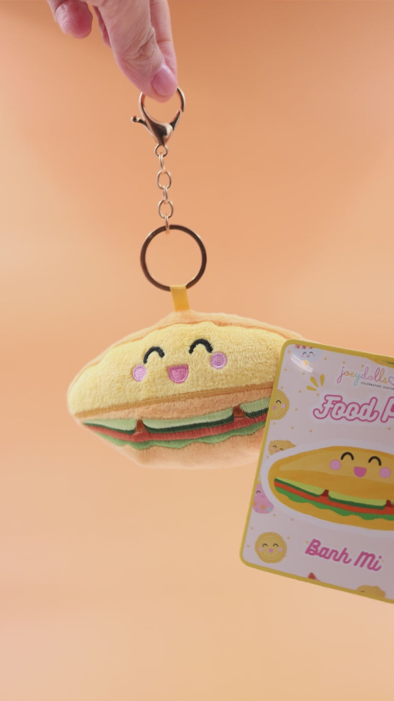 Vietnamese bánh mì Food Pals keychain being squeezed and rotated to show its soft texture, with a gold clasp and product tag