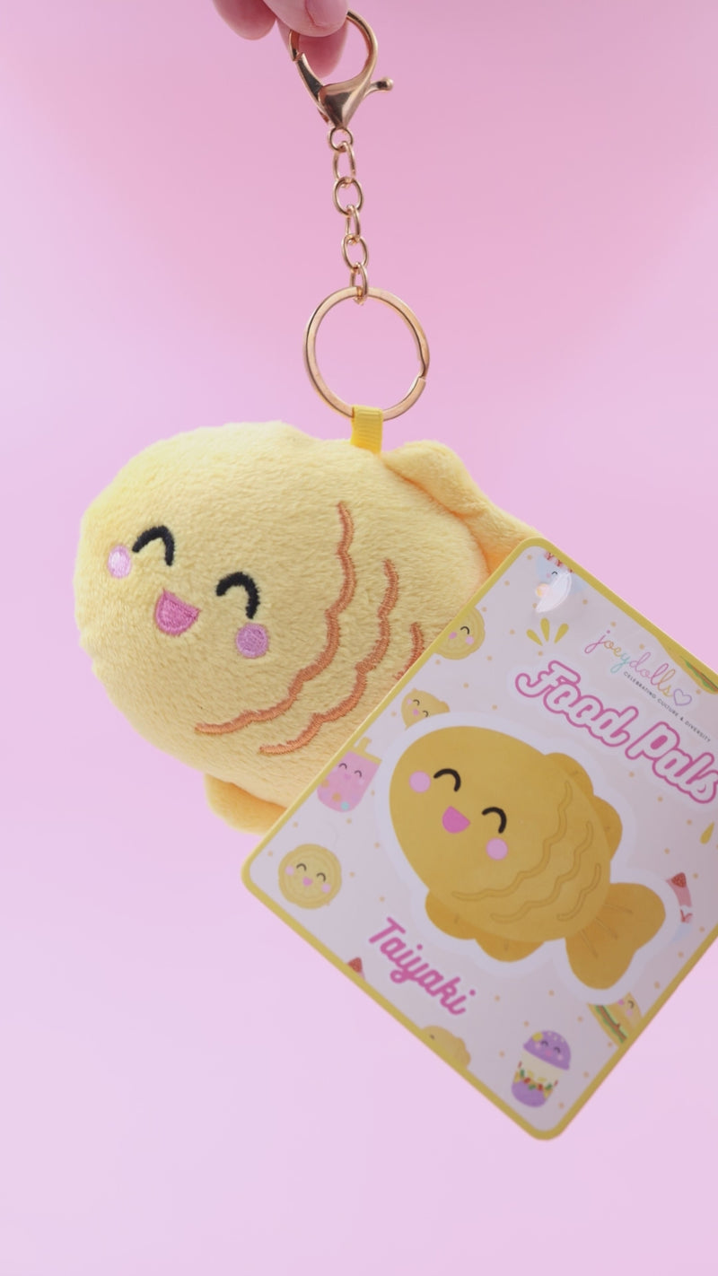 Japanese taiyaki Food Pals bag charm being squeezed and rotated to show its soft texture, with a gold clasp and product tag