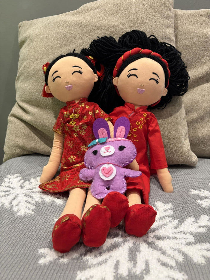 Customer photo: two Joeydolls Signature dolls in red outfits on a sofa with a purple plush bunny